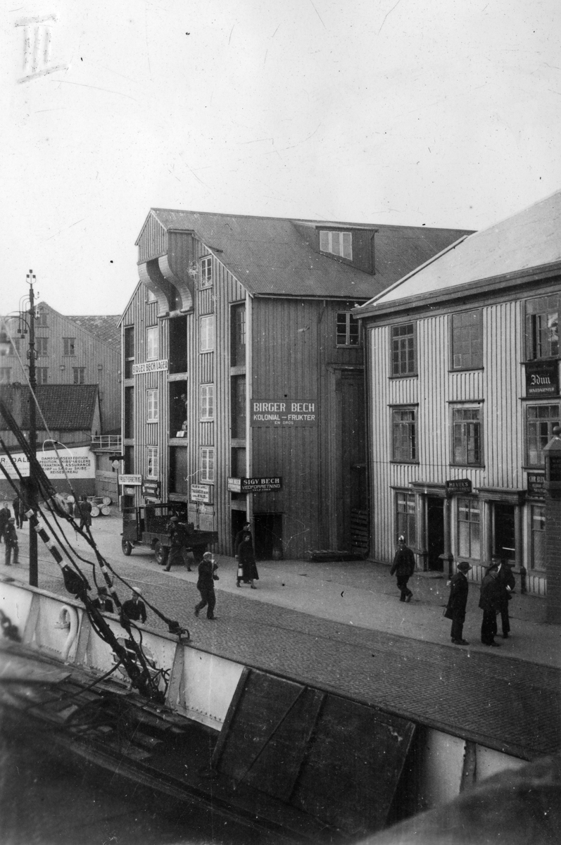 Gatebilde med forretningen Karen Strand, Birger Bech lager og Sigv. Bech vedforretning og kolonial i havnen i Kristiansund, 1935.