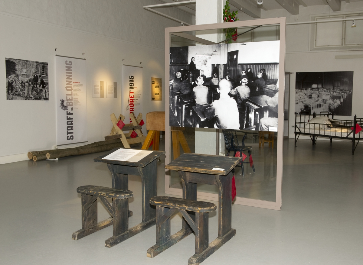 Utstillingsplakater med fotografier fra Bastøy skolehjem. Skolepultene er rekvisitter som ble brukt i spillefilmen "Kongen av Bastøy". Fra utstillingen om Bastøy skolehjem på Norsk Folkemuseum. Utstillingen stod i perioden 15.12.2010 til 31.12.2011.