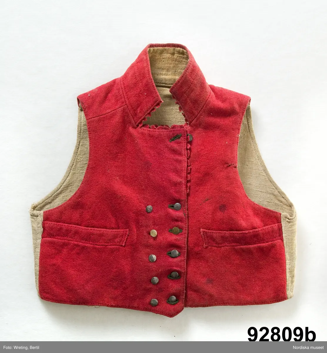 Mansdräkt i flera delar a-d.

a. Rock av svart vadmal
b. Röd väst
c:1-2 Vita strumpor
d. Knäbyxor av sämskskinn
Katalogkort finns.

a. Långrock av svart vadmal. Framstyckena/sidstyckena helskurna, ryggstycket smalt och kort,  avkuret i midjan, rikt veckat bakskört försett upptill med två ulltofsar och med pikerade klaffar en vid var  sida om skörtet. Svängda ärmar med 2 sömmar och blindslag med sprund oknäppt med 2 hakar och hyskor. Ståndkrage. Skoning av hemvävda ylleband i flera färger längs livets insidor, knäppning med hakar och hyskor.
"Dylika rockar tillhörde högtidsdräkten, vid mindre fester och till kyrkan brukades grå rockar af liknande snitt, ett snitt som gaf anledning till benämningen ´fiolen´för nysockenströjans ryggtafla ".
b. Väst av röd vadmal med ryggstycke av grovt oblekt linne i spetskypert. Hög ståndkrage och utvikta slag, med en uddklippt vadmalsremsa i kanten, dubbelknäppning med  vitmetallknappar, fästa på insidan med skinnremsa, knapphål tränsade med grönt ullgarn. 2 sidfickor med list. Foder av oblekt linnelärft, på kragens insida en bit av ryggtyget mitt bak.
c:1-2 . Strumpor slätstickade i tvåändstickning av fint vitt 1-trådigt ullgarn. Uppläggningsvarvet med rött och vitt ullgarn,  smal mönsterstickad överkant. Häl och tå av annat naturgrått garn. Mitt bak en sömmarkering med en avig maska. Vid anklarna broderade rombiska figurer i genombrutet mönster, kallas "löver" i rött ullgarn.
d. Knäbyxor av gult sämskskinn, med bred lucka med 5 knapphål, midjegjord knäppt med 2 knappar. Knapparna är av flera olika sorter av mässing, en av hängselknapparna av horn, 2 bak saknas. Midjegjorden fodrad med linnelärft. Knäsprund knäpps med 4 hakar och hyskor. Flikar vid sprunden uddklippta.
/Berit Eldvik 2010-01-08
