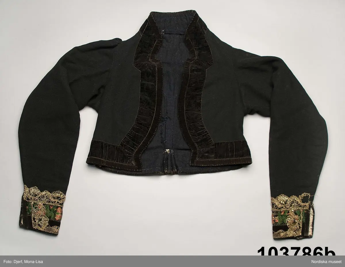 b. Brudtröja av svart vadmal,  Runt alla kanter bård av ytterst brunsvart sammetsband och innanför ett 4 cm brett svart sammetsband  med invävt bladmönster. På ärmarna ett svart slätt sammetsband med pålagd guldspets därefter siden band i rosa och grönt på botten av  svart  sammet och överst i bården en knypplad guldspets. 
c: Förkläde. Material: Textil, bomull. Teknik: Manufakturvävning. Handsömnad. Längd: 77 cm. Bredd: 110 cm. Färg: Vit.
Förkläde i vitt manufakturvävt bomullstyg, ihopsytt i mitten, smalrandigt, stärkt. Rynkningar mot midjelinning i tuskaftat bomullstyg, 1,5 cm bred, fastsydda bomullsband i sidorna. Uppvikt fåll nedtill, 6,5 cm, ovanför fåll, 5 lagda veck med ca 1 cm mellanrum, enkel utdragssöm i kanten av vecken.
/Inga-Lill Eliasson 2008-02-25

e: Krage. Längd: 47,5, cm - totallängd, bröststycke. Bredd: 33 cm - bröststycke. Höjd: 14 cm - kraghöjd, inkl spets. Material: Textil, bomull. Lingarn - spets. Bomullsgarn - broderi. Teknik: Tuskaft. Vitbroderi, Knyppling. Handsömnad.
Krage i tuskaftat vitt bomullstyg. Rektangulär duk, uppklippt halshål med fastsydd krage, 14 cm hög. Kragen har 3,5 cm bred fåll, enkel utdragssöm i kanten. Vitbroderi  i framkant,  plattsöm och kantsydda hål med infällt tyll, två sydda knapphål. Handknypplad spets fastsydd på långsida och korstsidor, 2,5 cm bred. Öppning fram, 24 cm långt sprund. Kragen är handsydd.
Lästips: Svensson Sigfrid, (1935). Skånes Folkdräkter, en dräkthistorisk undersökning 1500 - 1900. Stockholm: Nordiska Museets Handlingar: 3.
/Inga-Lill Eliasson 2008-02-19