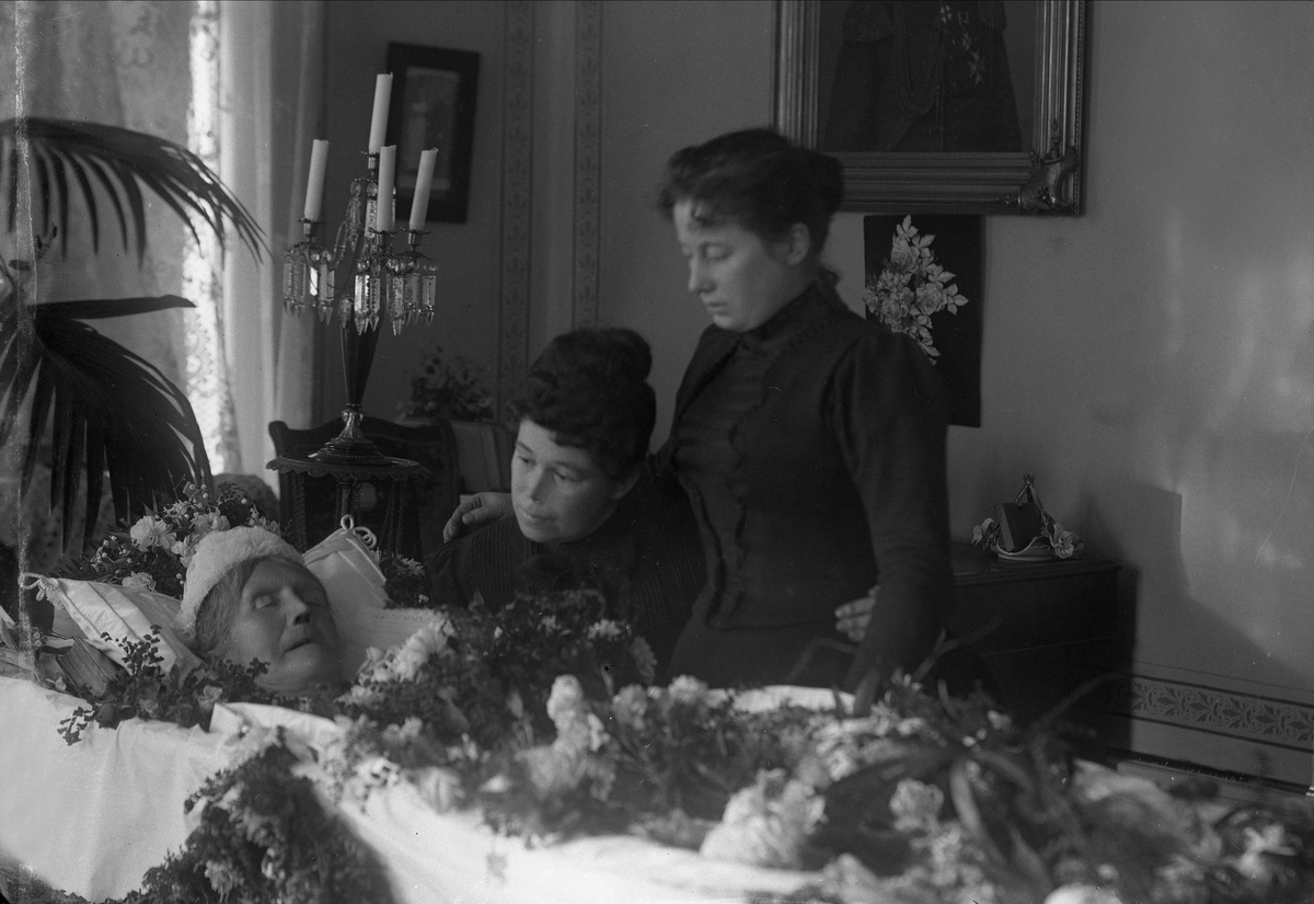 Post mortem-fotografi. Kvinne i pyntet kiste, siste farvel fra to kvinner/familien.