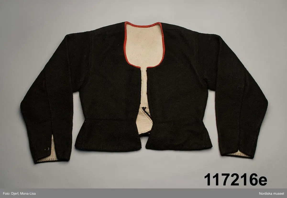 Huvudliggaren:
"Sorgdräkt för kvinna. Särk med 'hängseltåg', 'särkyvdel'; vit -'häsklä'; blått livstycke; svart tröja; huvudduk; 'svart näsduk'; hatt; 'raskförklä', 'sockar',  'hårbandsvifsa', huvudbindel."

Bilaga:
a: "8 Särk, övdel. av linne eller blågarn. med broderade linningar på överdelen"
c: "11. Hvit häsklä."
Anm: Kung Kerstin Larsdotters resa i Floda sn Dalarna 24/2 - 8/3 1912. Innehåller förteckning på inköp av dräktdelar från Floda, inv nr 117 216 - 117 239. Här finns  tillverkningstid och beskrivningar på vissa av dräktdelarna.  I vissa fall nämns också utförligt på vilka helgdagar dräktdelen  användes.

Katalogkort:
a: Hängselsärk
b. Överdel av halvlinne vävt i kypert.
c.  Halskäde av småmönstrat bomullstyg, liknande kambris, vävt  i kypertvariation med drällmönster.
d. Livstycke av mörkblå kraftig vadmal,
e. Tröja av grov svart vadmal

i. 
 Mönstervävt band med upplockat mönster i rött z-tvinnat ullgarn på vit linnebotten, med hjärtan, kryss och rombformer, 2 band om vardera 124 cm har vikts och sytts ihop så att det ena bildar en ögla och det andra har fria ändar avslutade med en tofs i bandets garn.
Läs mer om dräktskicket i Floda i: Albert Alm, Dräktalmanacka för Floda socken, Nordiska museet, Sthlm 1930
/Berit Eldvik 2005-04-14