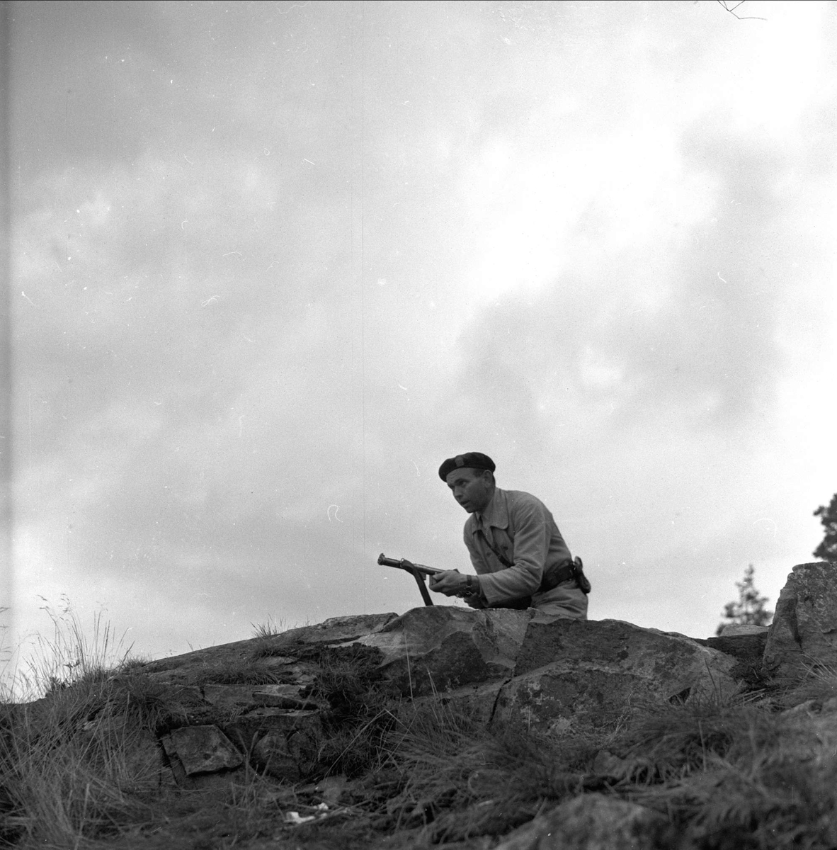 Politistudent med våpen. Oslo før 1954. Politiskolens trening i Gaustadskogen. Våpenet som politistudenten har skal være en Suomi M-37/39 maskinpistol. Kaliber 9mm parabellum.Våpenet er produsert av Husquarna i Sverige. Dette er en lisensproduksjon av den finske maskinpistolen med samme navn.