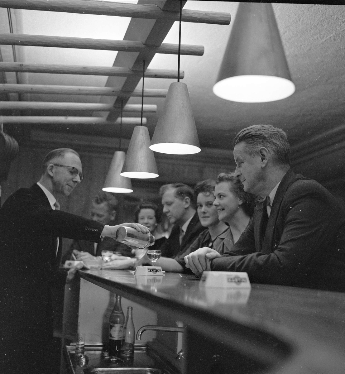 Servering i baren på Røros høyfjellshotell i 1959. Hovmester Vinnann, Leif Wahl og hotellets direktør Åslund i midten, antakelig. 
Sør-Trøndelag