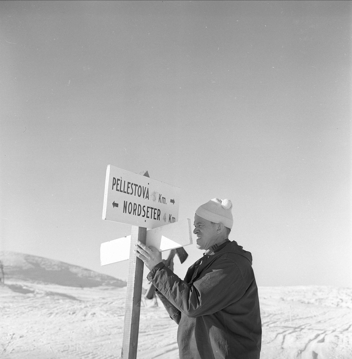 Øyer, Oppland, 25.03.1964. Portrett av Pelle på Pellestova ved skilt.