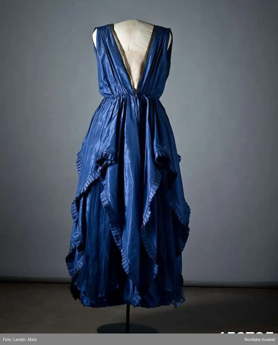 Ordered by Dora Lamm née Upmark (1880–1959), lady of the manor with a keen interest in innovative art and fashion. Delivered 1919.
A silk taffeta and pleated chiffon creation with gold ribbon details. Dora Lamm was married to the art collector Carl Robert Lamm of Näsby Manor, Täby. She embraced the Arts & Crafts movement and knew many artists such as Carl and Karin Larsson.