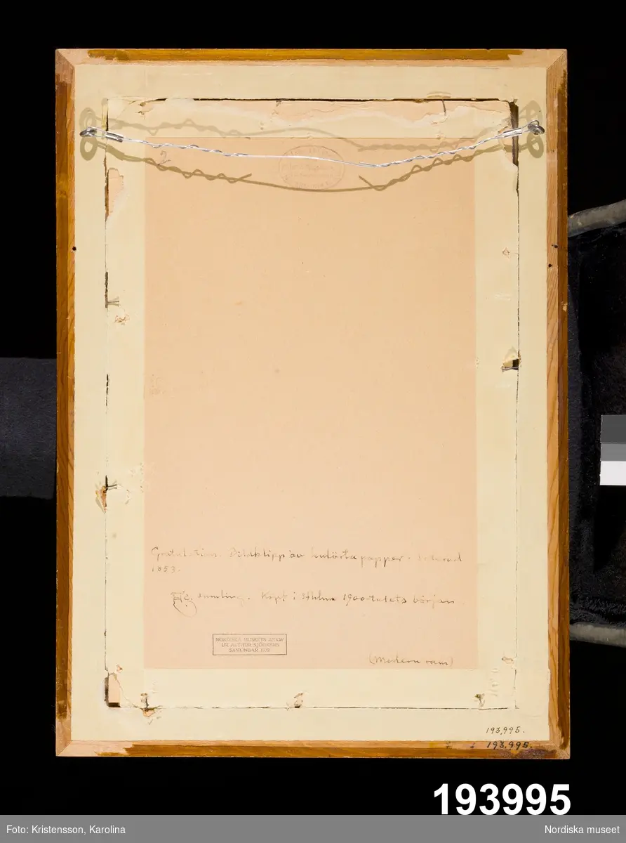 Minnestavla. Blomsterurna på fot flankerad av två män med kransar i händerna.