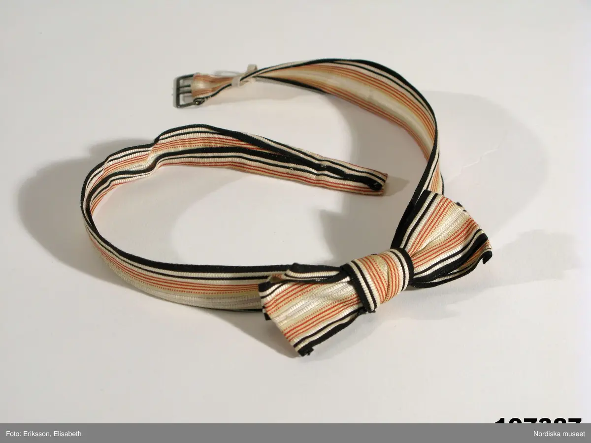 Fluga av siden. Ränder i svart, rött och beige.