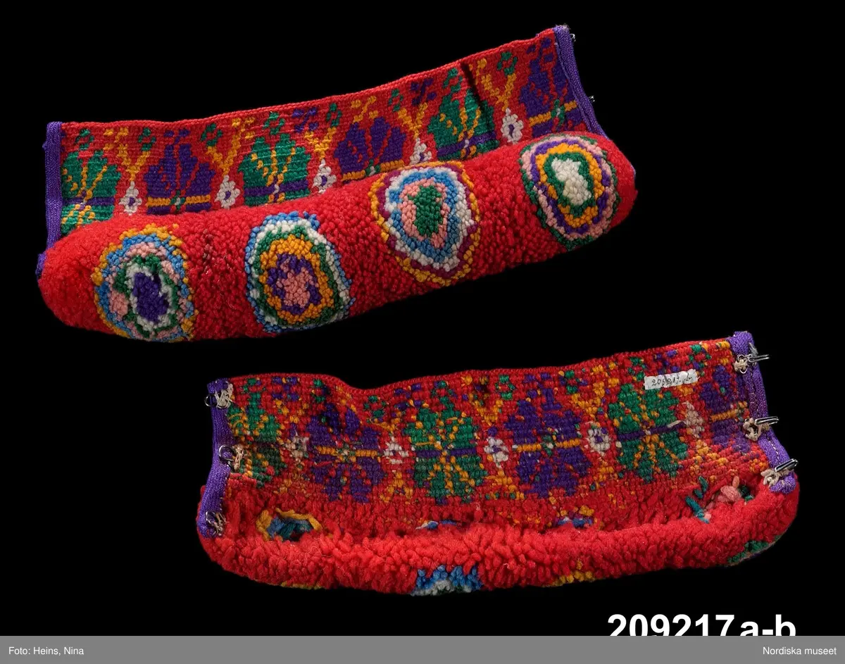 A-B. Muddar för man, ett par.
Maskinspunnet ullgarn, ylleband, hakar och hyskor.
Muddarna är virkade med fasta maskor med nedtag i bakre maskbågen i s.k. flerfärgsvirkning.  Mönstervirkningen görs hela tiden från rätsidan och garnet tas av för varje nytt varv. Kortsidorna är kantade med lila ylletrikåband, på den ena en rad maskinsöm. Det täta flossabrämet är sytt direkt i virkningen tråd för tråd och sedan formklippt. Knäpps runt handleden med tre svarta hakar och hyskor.
Färgerna är starka och opåverkade trots att det är kemiska s.k. anilinfärger som vanligtvis bleks mycket lätt.
/Berit Eldvik 2002