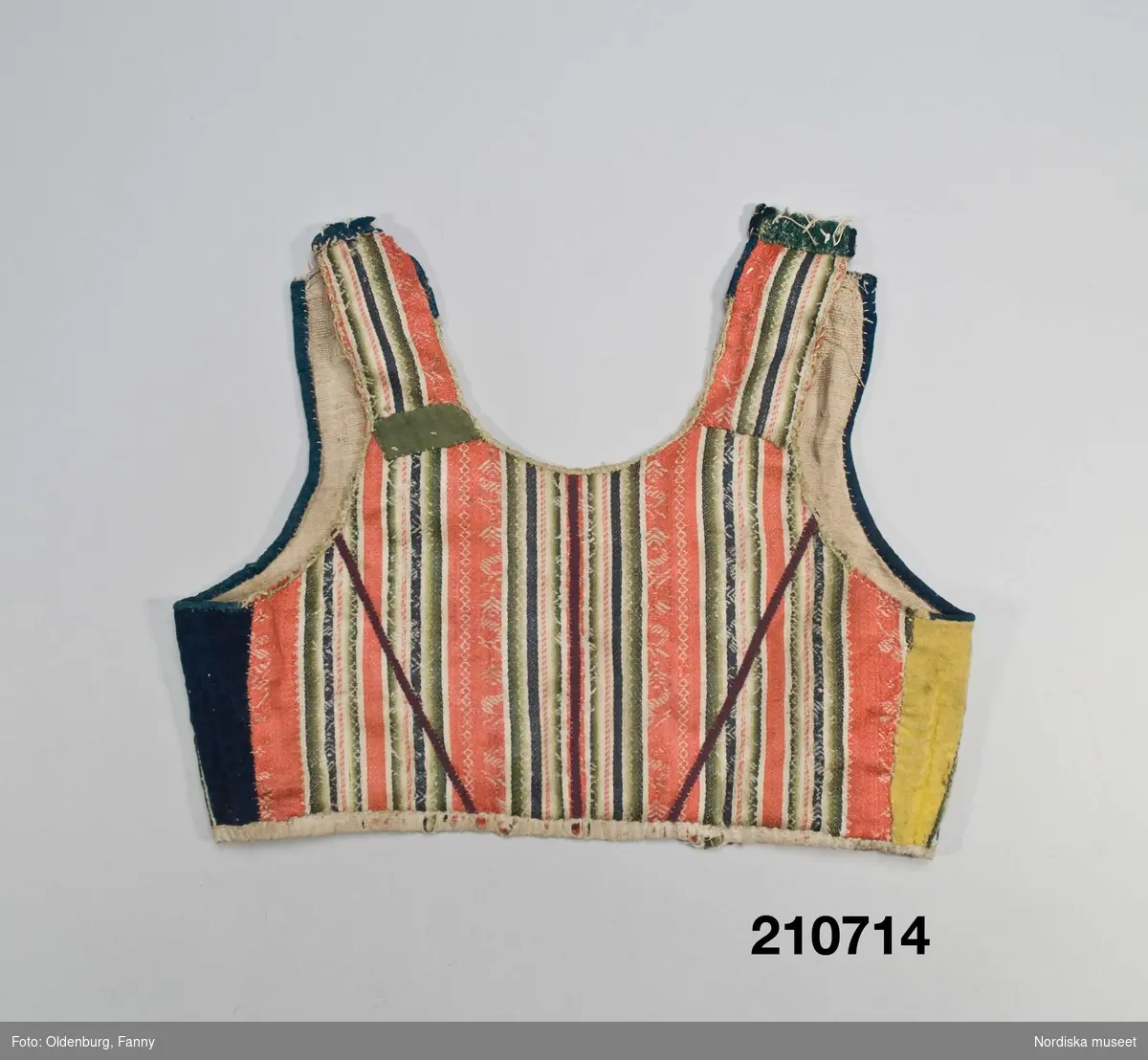 Livstycke "bod" som varit fastsytt på en kjol. Av varprandig yllesatin i rött, blått, vitt och gröna nyanser med invävda vita mönsterbårder, kvaliteten kallas blommerad kalmink och vävdes av kamgarn och glättades. 2 framstycken  och ett bakstycke med 3 påsydda lila band i ryggen. Livstycket består av flera hopskarvade bitar, dels av kalminktyget dels av mörkblått kläde samt blått och grönt vadmal (på axlarna och vid ena framkanten där det även finns en brun bit).I sidorna iskarvad med på ena sidan gult kläde på den andra mörkblått kläde. Kantad kring ärmhål och hals/framkant med blå vadmal och blått kläde. På insidan av framkanterna svart kläde, knäppning med  2 par hakar och hyskor av mässing. Fodrat med oblekt ojämnt vävt linnelärft
Anm. Slitet, avklippt på axlarna där livet förlängts med öglor av dubbelt lingarn.
Sådana blommerade kalminker vävdes främst i England och kom till Norden under 1700-talets andra del och blev moderna i folkligt dräktskick. 
/Berit Eldvik 2007-09-20