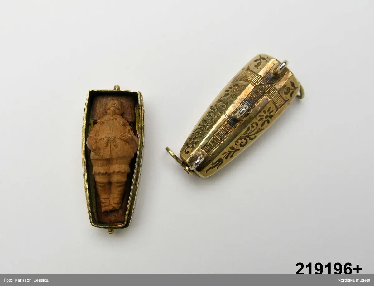Katalogkort:
"Smycke (berlock)
Silver
L 3,5 cm, br. 1,2 cm
I form av Gustav II Adolfs likkista. Trycklock med haspar. Graverad dekor. Miniatyrbild i trä av kunge, fäst i botten."