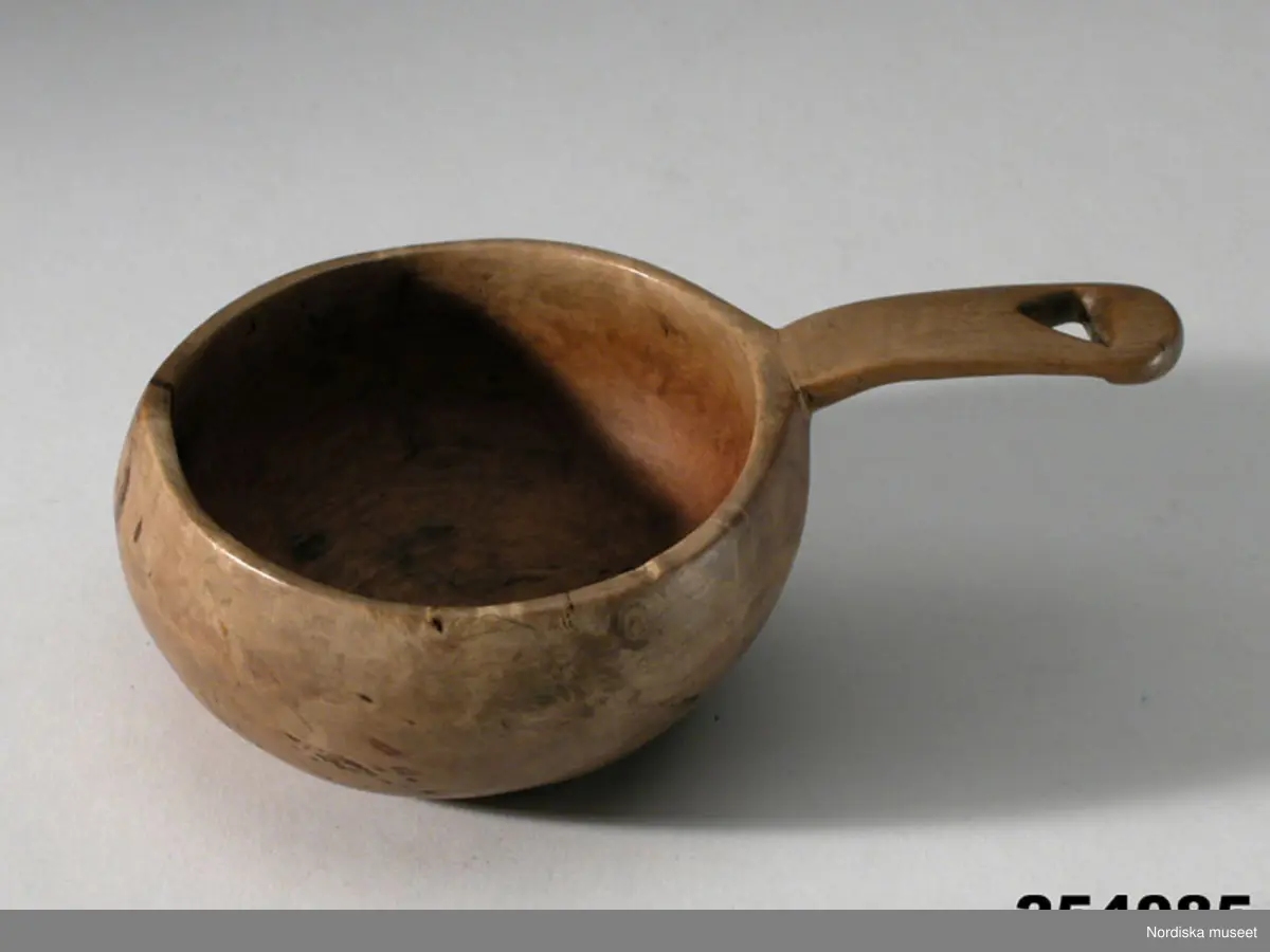 Huvudliggaren:
"Drickskopa 'kukse' av masurbjörk, hjärtformat urtag i skaftet. L 14 cm (med skaft), Diam ca 8 cm. I[nköpt] 11/3 1957 [från] Fru Maja Wickboms dödsbo gm major O. Wickbom, Stockholm jämte 254.083 - 098 [...]. [Brukningsort:] Lappland Torne lappmark."