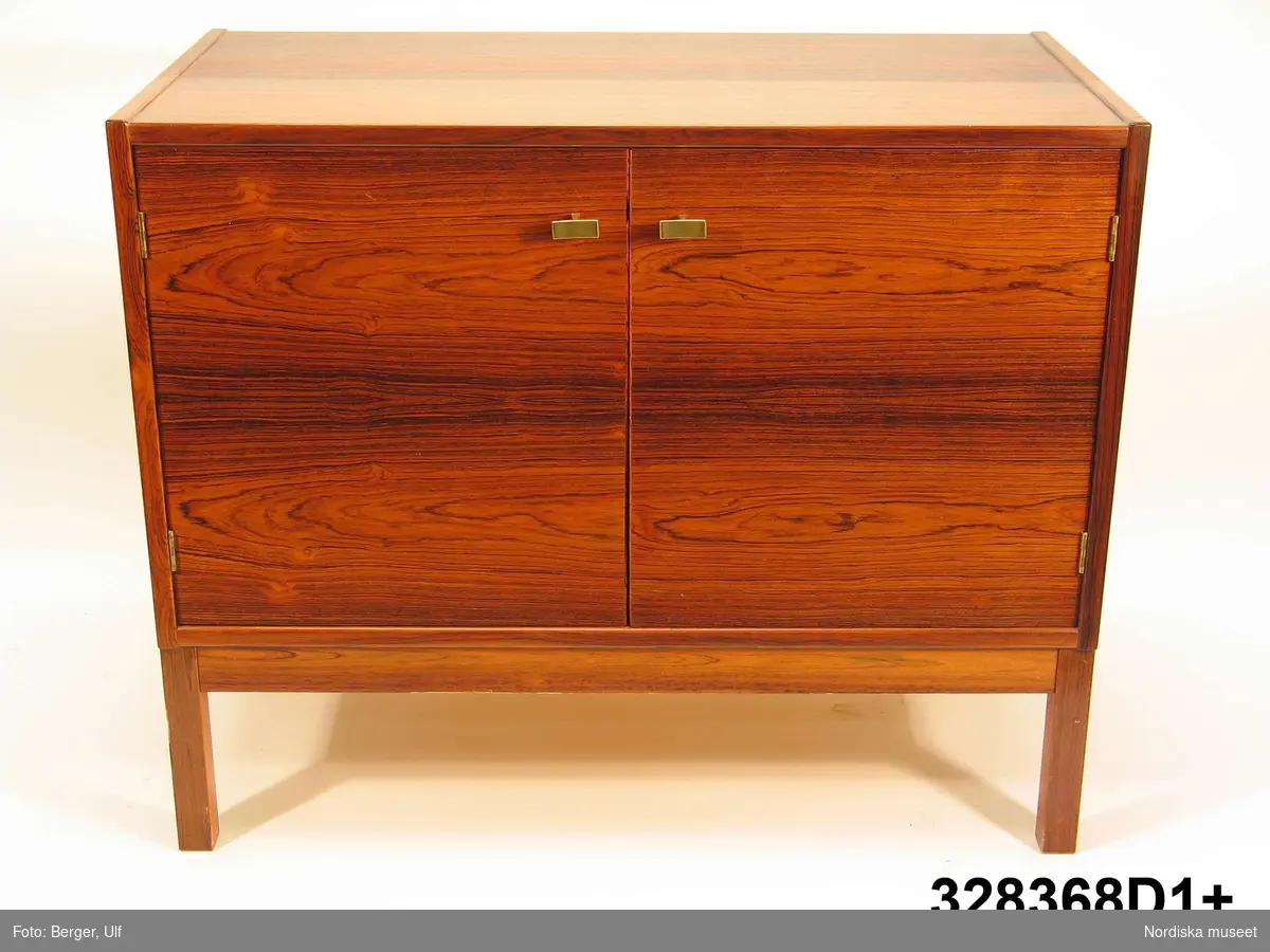 a-e:
Bokhylla, "Excellent",  med TV-bänk samt bar- och vitrinskåp, jakarandafaner på spånskiva, IKEA, 1968. 

Hyllan består av fyra sektioner med hyllor löst placerade på underredet. Skåp- och byråunderdelar med ryggar av masonit, fastnitade. Kvadratiska ben, fastskruvade i underredet. Lådsidor m.m. av björk och lådbottnar av vitlackerad masonit. Flyttbara hyllplan. Draghandtag och gångjärn av mässing.  Enligt IKEA-katalogen 1968 är ytan plastbehandlad.

Hyllan uppställd, från vänster till höger:
a:1+) Skåp med två dörrar samt a:2+) hyllöverdel, ett fast och två flyttbara hyllplan. Överst vitrindel med två skjutdörrar av glas (höjd 53,5 cm, bredd 41,5 cm).
b:1+) Byrå med tre lådor samt b:2+) hyllöverdel med tre flyttbara hyllplan. 
c:1+) Tv-bänk med en låda samt c:2+) hyllöverdel med tre flyttbara hyllplan.
d:1+) Skåp med två dörrar samt d:2+) hyllöverdel med 1 flyttbart hyllplan. Överst vitrindel med två skjutdörrar av glas (höjd 53,5 cm, bredd 41,5 cm), därunder ett barskåp med spegel som bakvägg, utrymme för flaskor till vänster och två glashyllor (48 x 19,5 cm) till höger. Barskåpet med fällbar klaff med lås. Belysning monterad i skåpets överkant.
e) Nyckel till barskåpets klaff. L 4,3 cm.

Möbeln har använts av givarinnan, Berith Helldén, f. 1945, hemmafru, och hennes man, Lars-Göran Helldén, f. 1946, inköpare, Tungelsta. Paret gifte sig 1967 och bodde som nygifta i en liten lägenhet i Borås. När de fick möjlighet att flytta till en större lägenhet i samma stad, utökades vardagsrumsmöblemanget. Hyllan inköptes 1968 på IKEA i Älmhult. Enligt IKEA-katalogen 1968 kostade de fyra hyllsektionerna totalt 2484 kronor. Hyllan har använts som förvaringsmöbel i vardagsrummet i Borås och i familjens nuvarande bostad i Tungelsta fram till våren 2005, då den inköptes av museet.

Hyllans innehåll har dokumenterats och en utförlig intervju med Berith Helldén har gjorts 2005-05-09 (se arkivreferens).
/Anna Womack 2005-10-18
