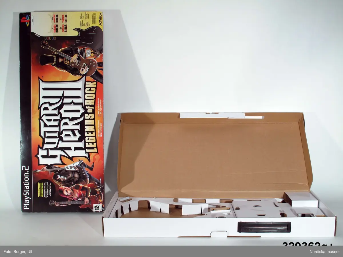 TV-spelet "Guitar Hero III Legends of Rock" med förpackning. 
a+) Elgitarr med avtagbar hals, av svart plast, svart axelrem av syntettextil med konstläder (plast) och plastöglor.
b+) 2 ark med klisterbilder att fästa på gitarren
c) Broschyr med instruktioner om funktion och säkerhet på flera olika språk.
d) Fodral av blå plast med inplastat omslag av papper med text. På framsidan "Playstation 2 / Guitarr Hero III LEGENDS of ROCK" och bild på hårdrockare. Baksidan bl.a. "SLÄPP LOSS DIN INRE ROCKLEGEND / Över 70 rockiga låtar.".
e) CD-skiva med programvara (förvarad i fodral d).
f) Instruktionsbok på de nordiska spårken (förvarad i fodral d) 
g+) Förpackning av papp. Ytterfodral med text och bilder. Inre lådan med inredning för de olika delarna.
 
Tv-spelet är avsett för spelplattformen Playstation 2, vilket är en vanlig spelplattform. Spelet går ut på att det spelas upp en låt (man väljer själv låt och nivå) och ska sedan försöka spela på gitarren genom att trycka på knapparna och på så vis lyckas spela samma ton som musiken spelar samtidigt.

Vid förvärvet avlägsnades plastpåsar som del av a och b låg i, samt två 1.5volts-batterier av märket Duracell som låg i gitarren, då de ej bedömdes möjliga att spara. Även fyra papperspåsar med Silicagel (för att hindra att fukt skadar elektronik mm) togs bort.

Nyinköp den 2008-02-20 för att rekonstruera julkklappsönskemål julen 2007 från Erik Thomelius född 1999, Vaxholm. Inköpt av Nordiska museet för 439 kr. Ingår i projektet "Barn tar plats". Se dokumentation i arkivet D455.
/Ulf Hamilton 2008-05-27     