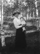 Anna Bergström i lång kjol, blus med brosch i halsen och hatt. På armen bär hon barnet Stig Trogen f. 1917