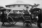 Skansen. Vårfesten 1899. Ett ekipage i öppen vagn. Några glada personer sitter i vagnen, en kusk sitter på kuskbocken.