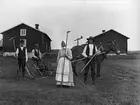 Skördearbete vid Ytterturingen, Haverö sn, Medelpad.  En man och en kvinna med räfsor i händerna, en man sitter på en slåttermaskin, en sk självavläggare, vilken är spänd för en häst.