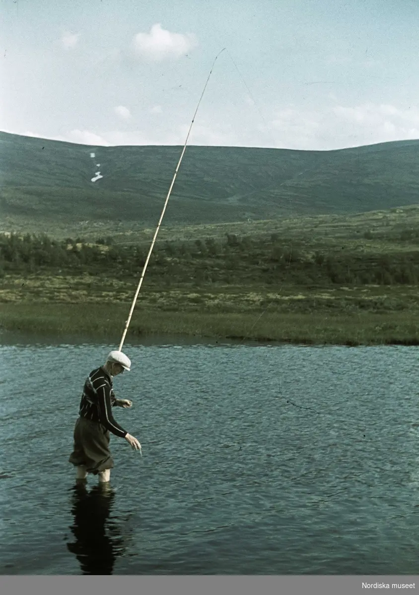 Landskap med en man som fiskar. I bakgrunden fjäll.