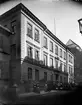 Exteriörbild från Lärarinneseminariet, Riddargatan 6, Stockholm. Buggnaden ritad av Gustaf Sjöberg och uppförd 1871. Utanför på trottoaren går en grupp unga kvinnor, troligen 1910-tal.