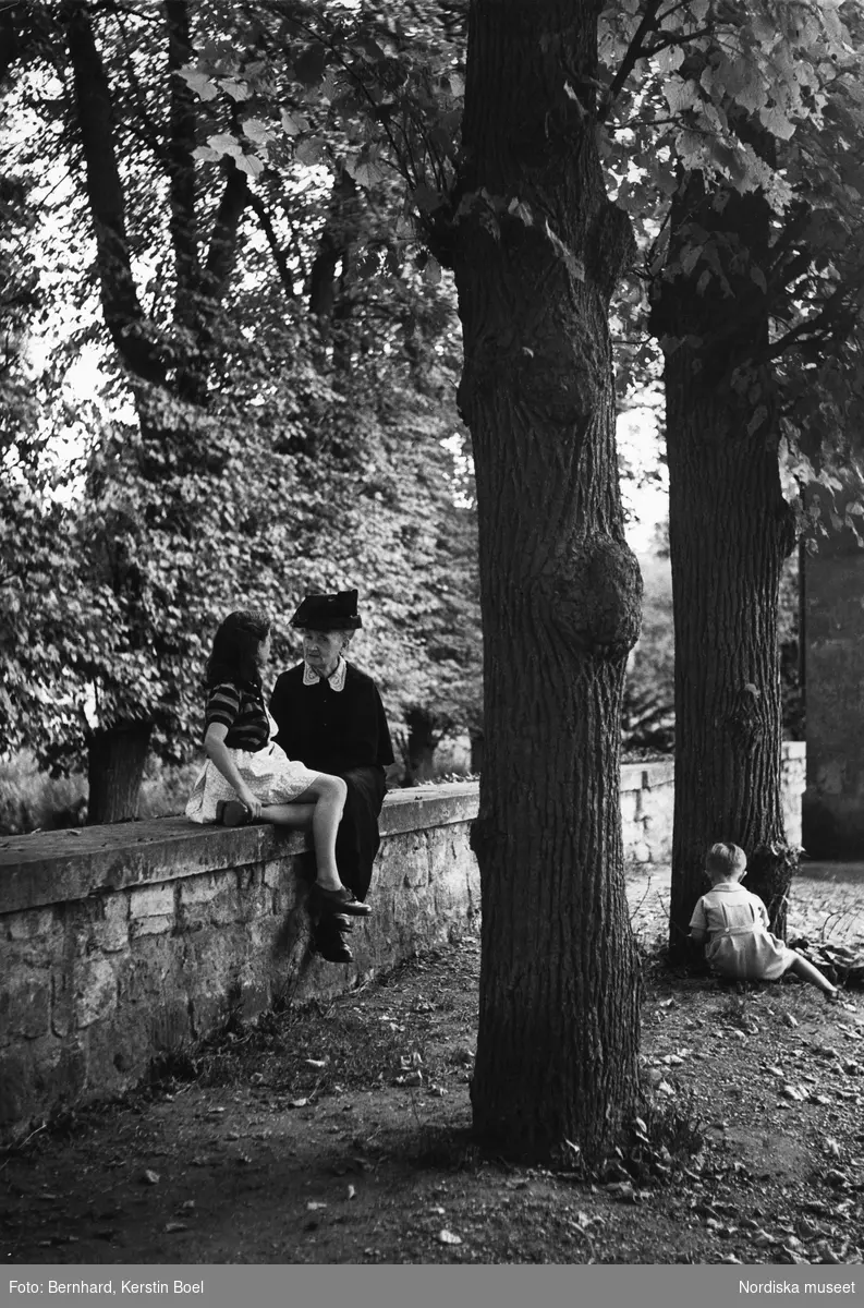 Äldre kvinna och ung flicka sitter på stenmur i slottsparken vid Malmaison, Frankrike