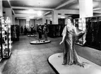 Interiör från Nordiska Kompaniet, damkonfektionsavdelning. Skyltdockor på podie. Kläder och accessoarer i glasmontrar.