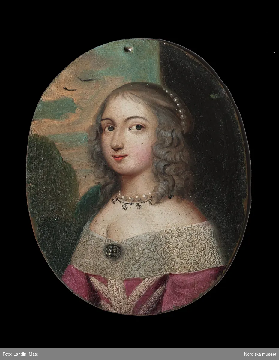 Katalogkort:
"Målning på kopparplåt, osign. Enligt uppgift av givaren föreställande en fröken Hahne. I fodral av svart pressat läder på stomme av papp med 13 glimmerskivor med målade dräkter och dräktdetaljer enligt uppg. målade av prof. N. H. Sjöborg (1767-1838)."
"Blont hår, mörkgrå ögon, rosafärgad klädning besatt med vita spetsar och spetskrage, vitt pärlband i hår och om hals, dessutom juvelhalsband och juvelbrosch. Bakgrund t.h. brunt draperi (vägg?) t.v. träd mot molnig blå himmel, 2 flygande fåglar. Kopparplåten genomborrad upptill. Till detta höra 13 st glimmerskivor att lägga på målningen. I svart ovalt etui, 88 mm x 73 mm av svart refflat skinn, invändigt klätt med ljusblått siden."

Genom att lägga de olika målade glimmerskivorna ovanpå porträttet förändras Kerstin Hahnes utseende. Skivorna visar enligt katalogkort:
- vit turban virad med gulbrunt, ljusbrun draperad dräkt med svarta prickar
- svart huvudbonad och gula örhängen
- svart huvudbonad, ljusröda örhängen, ljusröd bröstrosett
- svart hatt, svart kort jacka, vit krage och vita ärmar synliga i uppslitsningarna
- svart dok och klädning, vit krage
- ljusröd hårprydnad, örhängen vita och ljusröda, svart klädning med vit krage
- ljusbrunt hårnät, dito örhängen med vita pärlor, ljusbrun klädning med vita ärmar
- vitt nunnedok, svart dräkt
- ljusbrun hårprydnad, möjligen nät av band, vita örhängen, svart klädning, vit krage
- brun huva med krage, möjligen kappa
- svart barett med en grön, en vit och en rosafärgad plym, fästade med en gul agraff, vita örhängen, vit bröstrosett
- hårklädsel av 3 gula fjädrar samt en gul, en vit, och en grön plym, svart mask, vita örhängen, vitt band som täcker hakan, två gula bröstrosetter
- hårprydnad (nät?) ljusrött, röd och vita örhängen, till venster en neger, som omfamnar damen, under negerns huvud något gulvitt, som möjligen tillhör hans dräkt

Kerstin Hahne, död 1656, gift med Honorat Verdelet, var dotter till uppvaktaren hos kung Karl IX:s barn, Christoffer Hahne till Hesselby och Ingrid Björnsdotter.