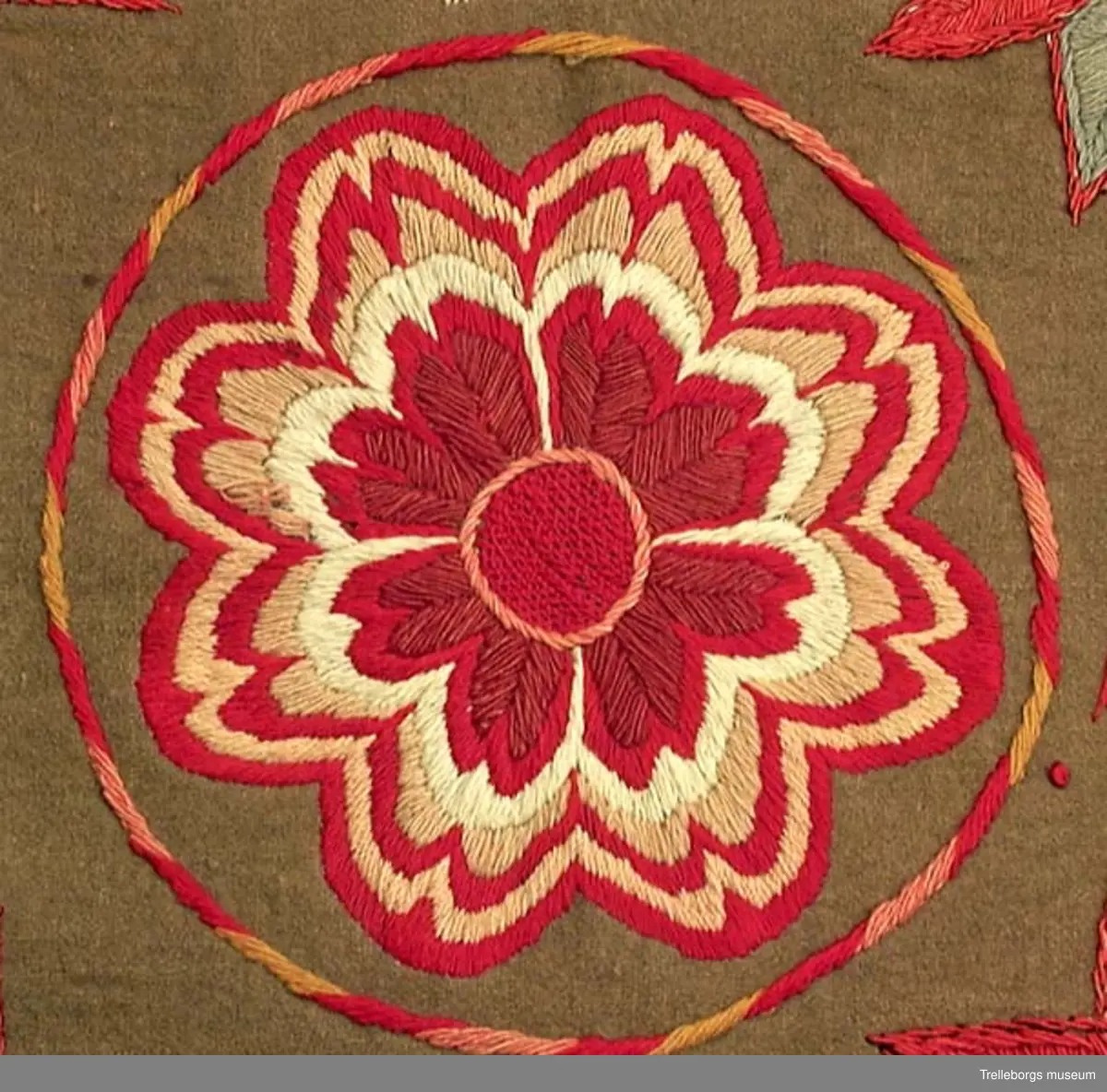 Bottentyg är grön vadmal. Tre stora ringar i kontur utgör huvudmotiv. I ringen i mitten är en stor blomma med 8 kronblad utfyllnad. I de båda ringarna vid sidan är broderat en spetsuddig stjärna med 8 vingpar. Dess centrum är en snedställd kvadrat, sydd i gallerliknande konstsöm. Utmed agedynans långsidor är broderat olika blomsterstjärnor, pionliknande blommor och en blomliknande rundning av 4 st hjärtfigurer. Färger: vitt, gult, svart, blågrått samt många olika nyanser i rött. Baksidan tegelröd yllevävnad. 
Enligt katalogen märkt I.W.D.S.  SL. Hjärtrosetter och hjärtan. 
Enligt Ernst Fischer, Årsbok från Malmö museum 1971, sid 180: En åkdyna i Tbgs museum har som mittmotiv en runduddig stjärna, omgiven av en ring samt en hjärtrosett över och under, flankerad av spetsuddiga stjärnor. T.h. och v om mittmotivet stora spetsuddiga stjärnor inom ringar. I hörnen varierande blomformer. De ganska svårtydda initialerna skulle kunna tydas som LWD IVH, ehuru bokstäverna då icke är placerade i rätt ordning. IVH skall i så fall beteckna I Vämmenhög.