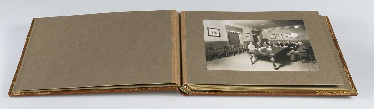 Album, inbundet i helfranskt band i brunt läder med stämplade ramverk och ornament i guld. På pärmens framsida spegelmonogram, komponerat av bokstäverna GEK (Gustaf E. Karlsson). Guldsnitt runt om, blad av mörkgrå kartong. Frontespis med textad tillägnan: "Till Direktör Gustaf  E. Karlsson 60-årsdagen 19 30/10 28. Med varm lyckönskan och tack för värdefullt arbete. Uppsala Specerihandlarförening". Albumet innehåller fotografier av Gustaf E. Karlsson, av hans speceriaffär, av styrelsen i Uppsala Specerihandlarförening samt av föreningens hedersledamöter och medlemmar. Albumet på pärmens baksida stämplat: "Levins Bokbinderi. Uppsala Bokband C W Bergman". Mapp, klädd med mörkbrunt läder. 
