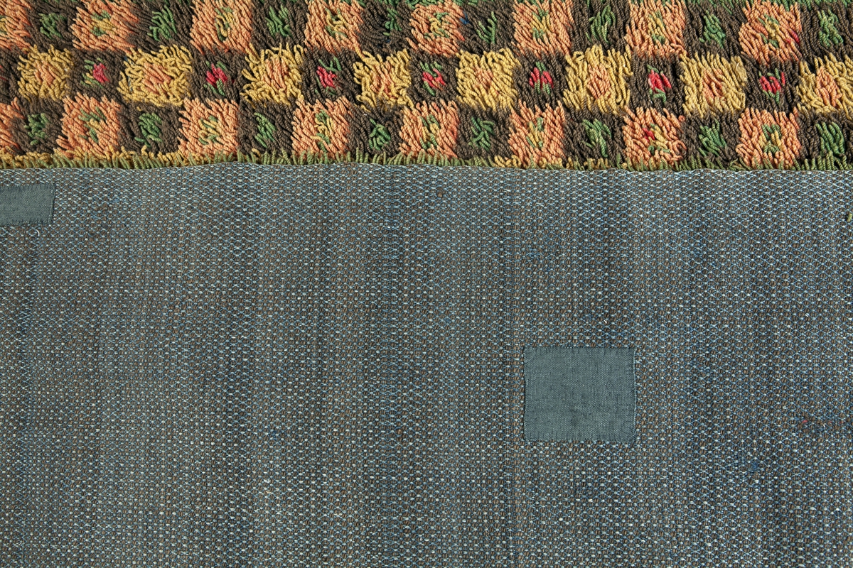 Prydnadsrya i två våder, hopsydda kant i kant. Botten i korndräll med varp av blått s-tvinnat lingarn 11 tr/cm och inslag av mörkbrun s-spunnen ull 7½ inslag/cm. Nockor av en tråd tvåtrådigt z-tvinnat hårdtvinnat ullgarn, knutna med giordesknut över 4 varptrådar med 4 varptrådar mellan nockorna och 4 inslag mellan nockraderna. Nockorna syns ej på baksidan.

Mönster: Stort blått mittfält avgränsat mot bården av en röd, en grönbrun och en gul smal linje. På det blå mittfältet, utmed sidorna romber av rött, grönbrunt och gult. Bred bård av schackrutor i grönbrunt, gult och rosagult. Gröna, röda och gula prickar i rutorna. Ytterst smal grön rand.