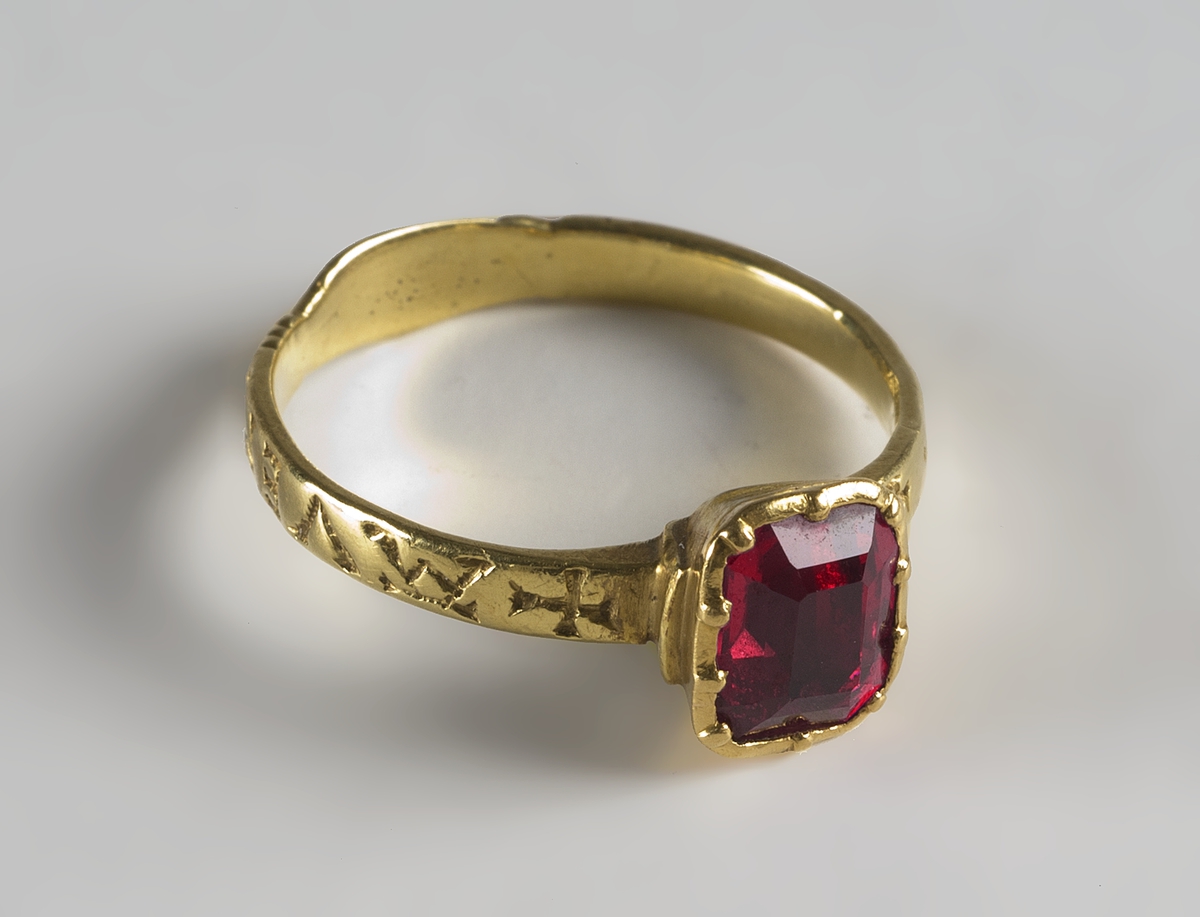 Fingerring av guld med infattad röd sten och handslag på skenans baksida. På ringens utsida ingraverat  AVEM ARIA ( d.v.s. AVE MARIA) och två likarmade kors. Tillhörande etui UM20676b.

Didners lät sätta in den ljusröda rubinen.