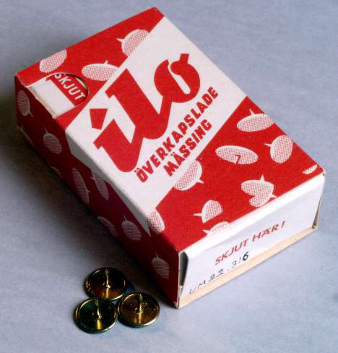 Skjutask av vit och röd papp med text: ilo, överkapslade, mässing, kvalitetsstiftet ilo, packat i praktisk "sparförpackning" till nytta för hem, kontor och ritsalar. Rosendahls fabriker AB, Filipstad.
Innehåller häftstift av mässing, se UM22316b.