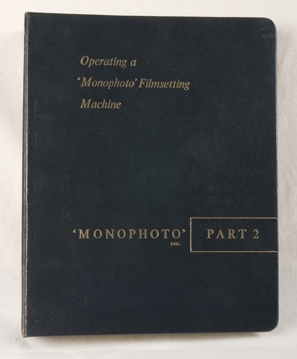Handbok: Svart ringpärm av tjock papp och med metallinsats. Texten på utsidan är i guldfärg. Handboken har titeln "Operating a 'Monophoto' Filmsetting Machine, PART 2". På försättsbladet står bland annat "THE MONOTYPE CORPORATION LIMITED Registered Office: Monotype House, 43 Fetter Lane, London, E.C.4 Head Office and Works: Salfords, Redhill, Surrey". I pärmen ligger flera lösa blad, däribland några ritningar. Några lösa blad verkar ha varit fasttejpade på olika sidor i pärmen.