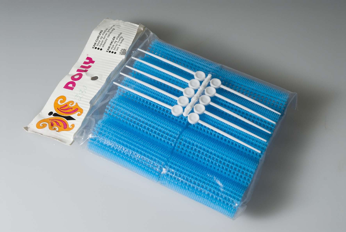 Originalförpackning av plast och papp innehållande 10 blå papiljotter samt 10 vita papiljottpinnar, allt tillverkat i plast. Förpackningen märkt: "DOLLY Kam-papiljotter Stöhr". Pris påskrivet med grön penna: 2.80.