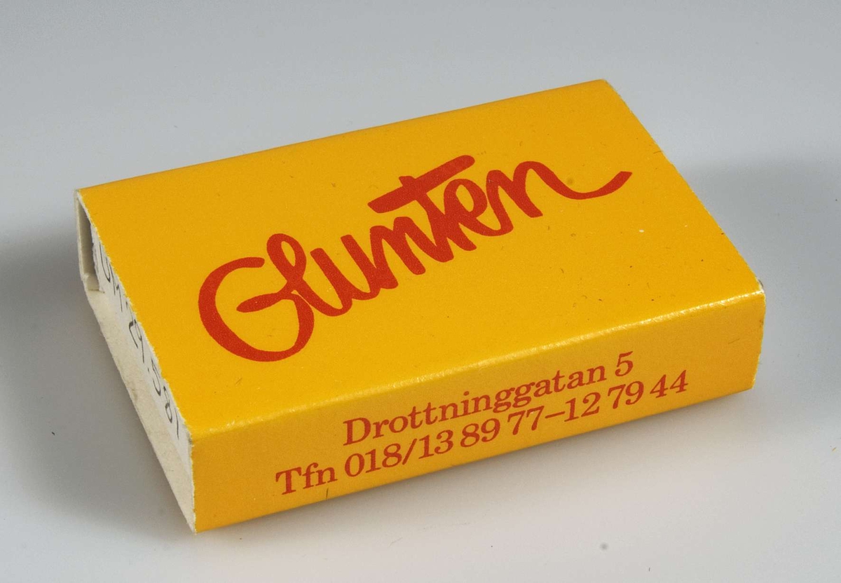 Gul tändsticksask med rött tryck "Glunten" samt på kortsidan "Drottninggatan 5 Tfn 018/13 89 77 - 12 79 44". Innehåller tändstickor.