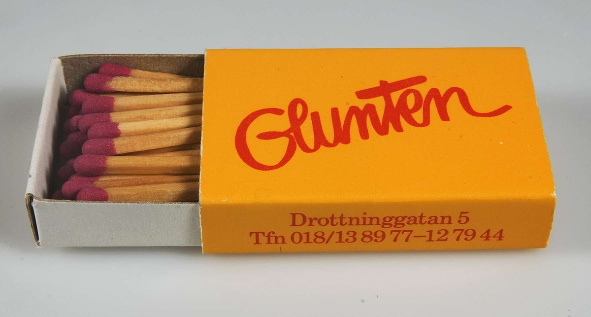 Gul tändsticksask med rött tryck "Glunten" samt på kortsidan "Drottninggatan 5 Tfn 018/13 89 77 - 12 79 44". Innehåller tändstickor.