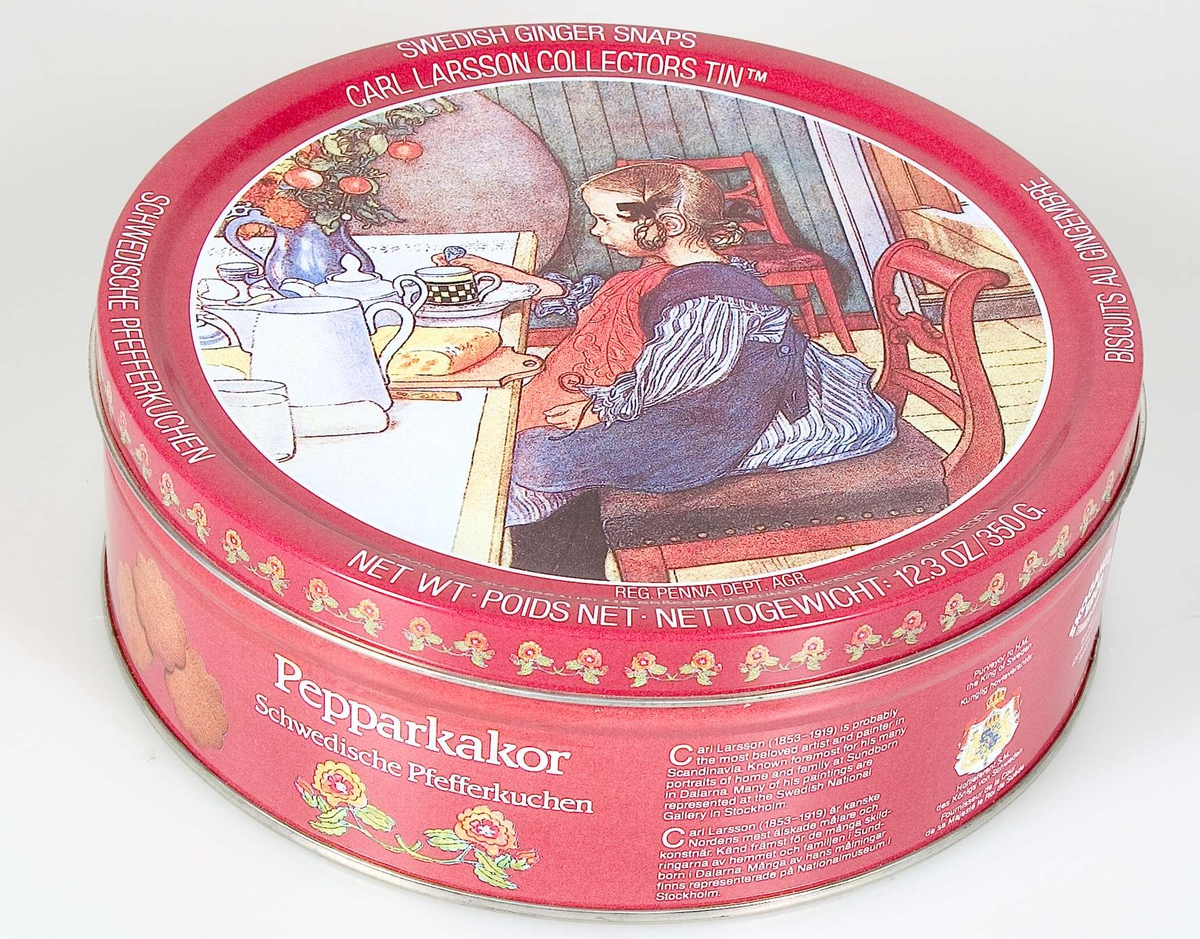 Pepparkaksförpackning av järnplåt. Mörkröd bottenfärg. Tryckt dekor: på locket en Carl Larsson-bild i färg och en bård av blommor längs kanten. På burken fotografiska bilder av pepparkakor samt blommönster. Text på svenska, tyska, engelska och franska, förutom ingredienser och andra varufakta, en kort text om konstnären Carl Larsson samt:  SWEDISH GINGER SNAPS, CARL LARSSON COLLECTORS TIN ... SKOGAHOLMS BRÖD...