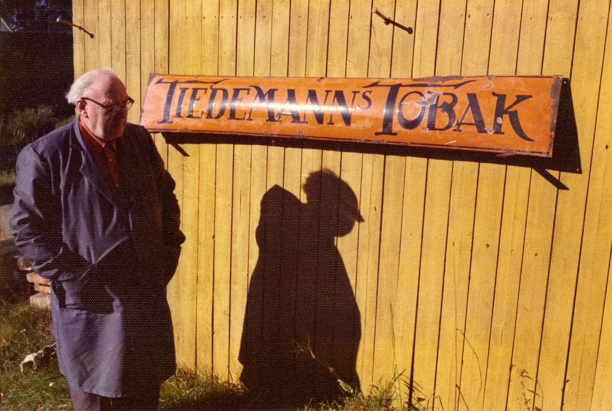 En mann står foran en gammel reklameskilt fra Tiedemann.