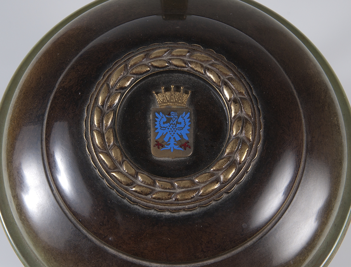 Idrottspris av brons i form av en dryckeskanna med lock, handtag och fyra fötter. Färgerna brunt och grönt. I botten stämplad Ystad-Brons MADE IN SWEDEN. På locket en krans och Uppsala stads logotyp i relief. På två av fötterna dekoration i relief: en springande man med fackla i ena handen. På kannans "framsida" finns inskriptionen: WOLMAR OHLSONS VANDRINGSPRIS ORIENTERING.  Dessutom inskriptioner med namn på pristagare och deras poäng från åren 1961 till och med 1972: 1961 Sven Olsson, 1962 Folke Tapper, 1963 Sune Berlin, 1964 Sten Andersson, 1965 Sixten Tapper, 1966 R Bromander, 1967 - 1969 Berthold Fredman, 1970 - 1972 Dag Kihlbom.