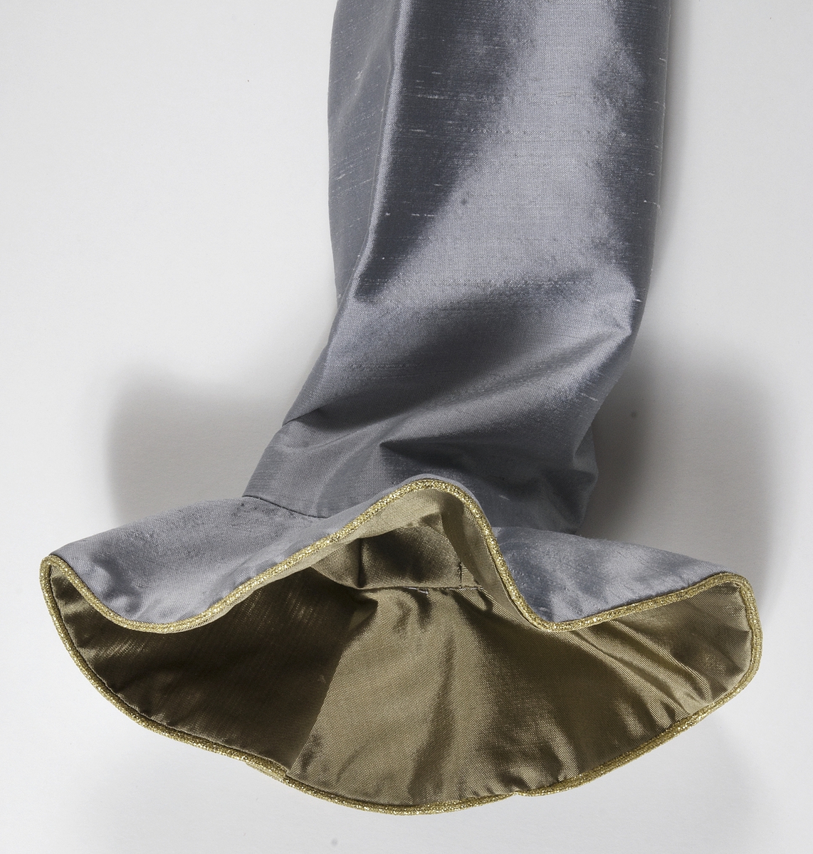 Klänning i grått siden. Figursytt liv. Broderier på framstycket med inslag av pärlor, lila garn och applikationer i guldfärgat och ljusgrått siden. Urringad hals kantad med guldband. På ryggsidan dragkjedja och hyska. Klänningen har smala långa ärmar som är klockade vid handlederna med infodringar av guldfärgat siden, kantat med guldband. Kjolen är utställd och har lagda veck i midjan. Längst ner på klänningen finns en cirka 30 centimeter bred våd av guldfärgat siden. Ovanför våden ett guldfärgat band. Klänningen är fodrad med grått fodertyg.