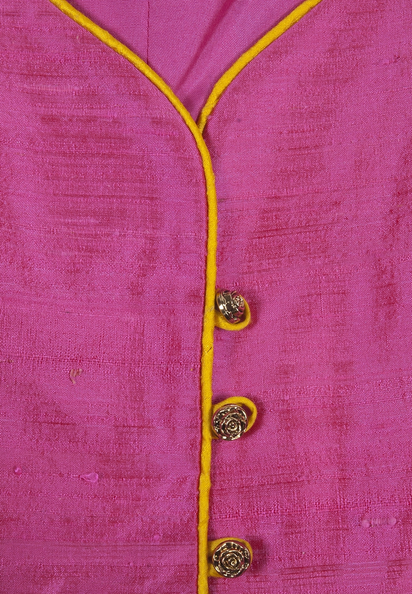 Ärmlöst liv i rosa siden. Livet är formsytt och kantat i gult siden. Livet knäpps på framsidan med agraffknäppning med fem guldfärgade plastknappar som har formen av rosor. Dessa är knäppta med agraffknäppning med öglor i gult siden.Livet är fodrat med rosa fodertyg.