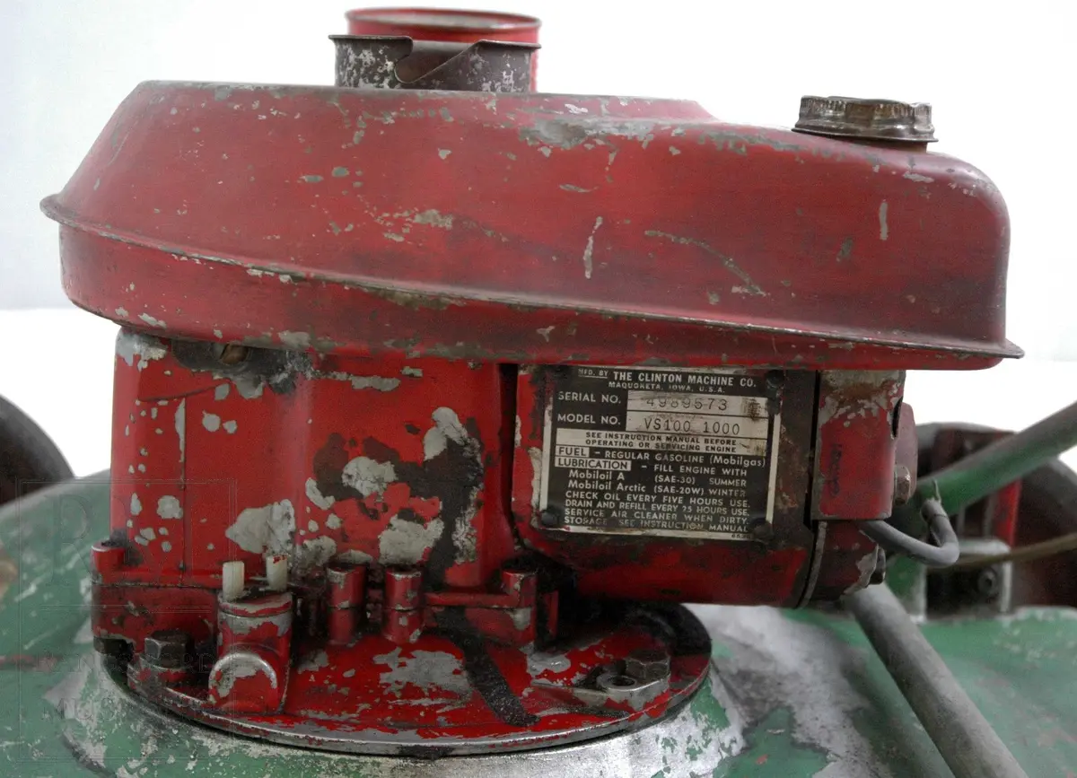 Gressklipper i aluminium med 4 gummihjul. Motor midt på. Motor har boks festet på siden. Metallhåndtak. Gresset blåses ut til høyre.