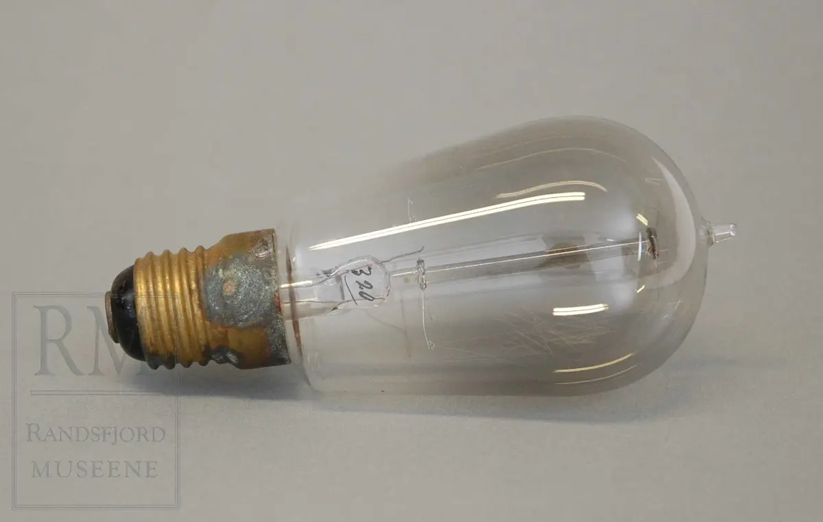 Til elektrisk belysning. Messingsokkel med gjenger. Glasset i kolben gjennomsiktig. Tupp i enden