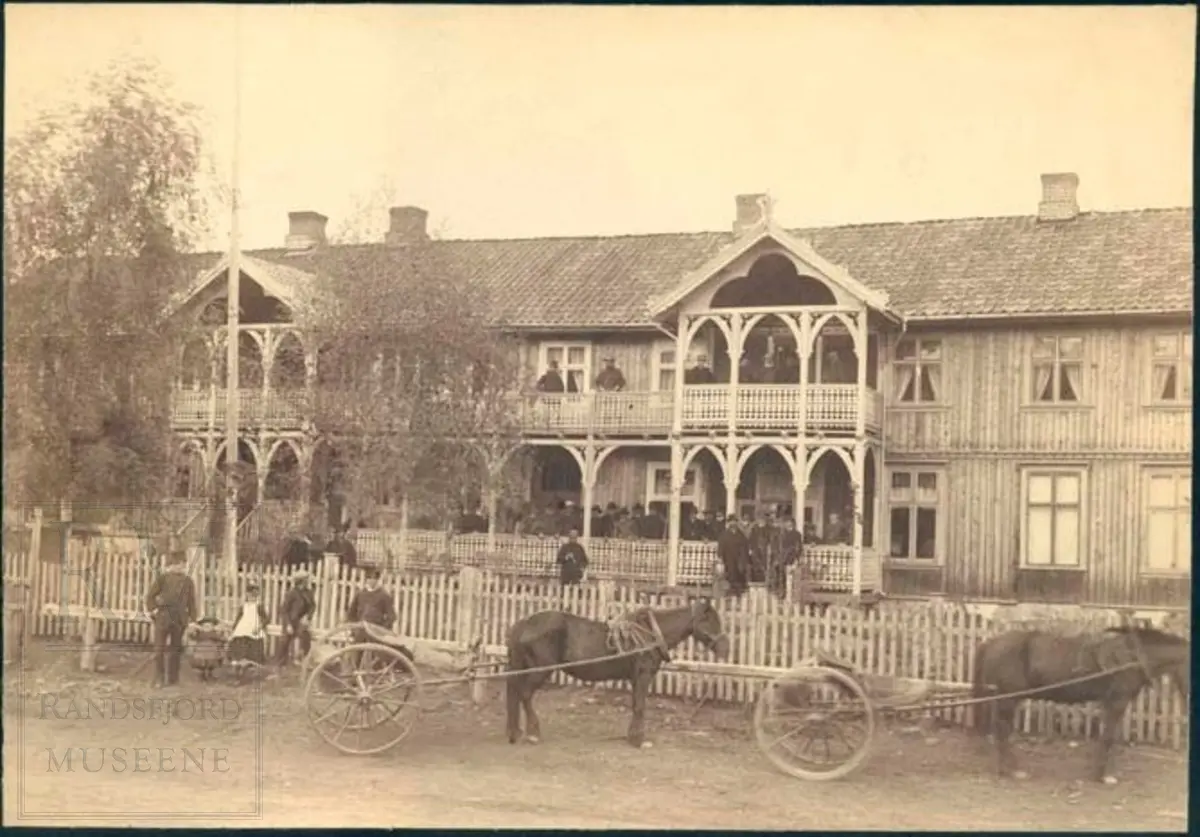 Augedalsbro Hotel, en gruppe fotografert på hotellets verandaer, to hester i gata.