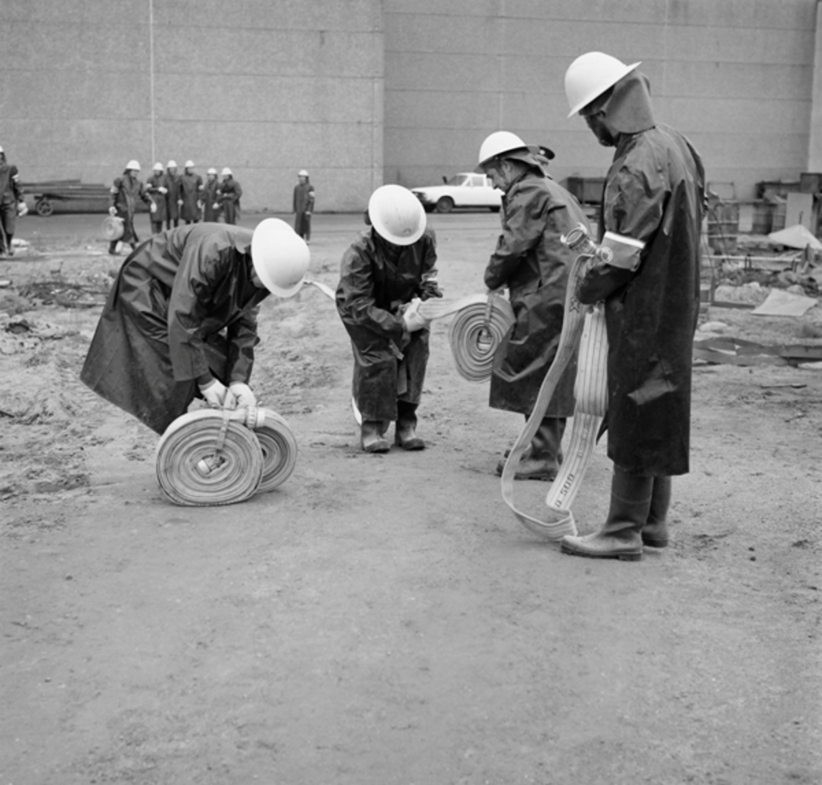 Brannmenn ruller opp brannslanger på en brannøvelse ved Kvernelands Fabrikk AS på Øksnevad 03.06.1975