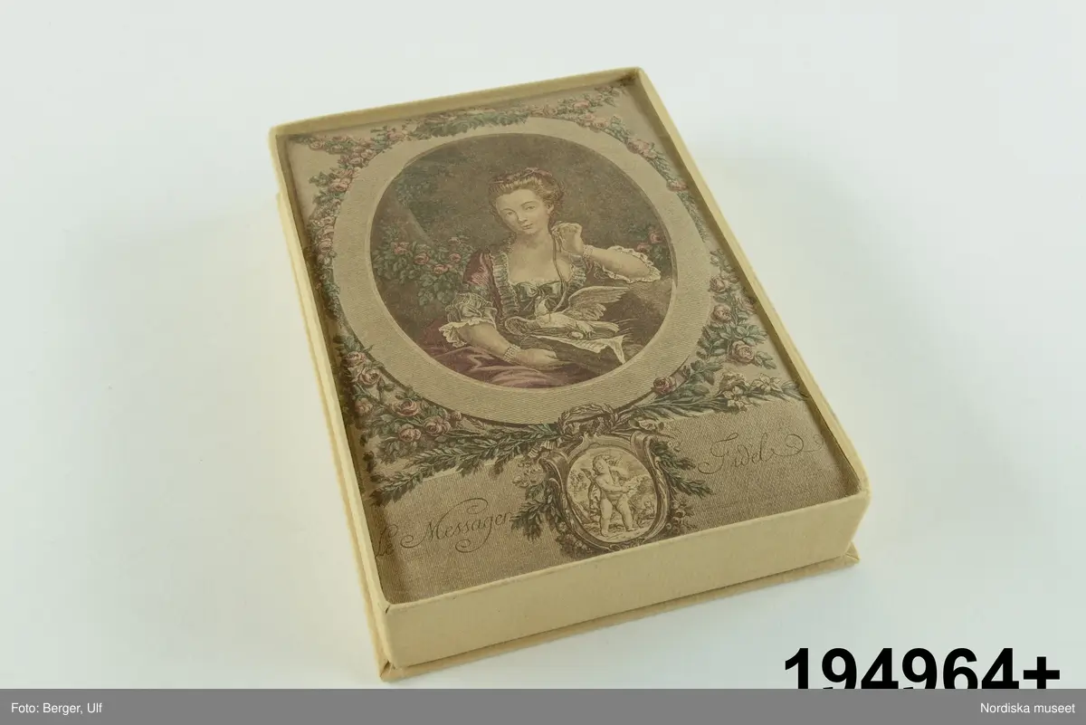 Huvudliggaren:
"Konfektask, kartong, rekt., trycklock; på locket bröstbild av dam och Amor; 'Le Messager Fidel'. Gåva 20/11 1933 av fröken Dagmar Landelius, Stockholm."

Bilaga:
"En samling föremål från Landelius Kungl. hovkonditori, Storkyrkobrinken 9, Stockholm, skänkta av fröken Dagmar Landelius. Givarinnans morfar, J. C. Landelius, öppnade 1858 affären på Storkyrkobrinken. På 1860-talet öppnade samma firma den s.k. paviljongen på Drottningholm, vilken ombyggdes 1903. Affärsrörelsen på Storkyrkobrinken drevs till 1910, då huset skulle rivas, varför huvudaffären flyttades till Strandvägen 7A samt en filial till 16 Storkyrkobrinken.
I den gamla affären skyltades med två speldosor (nr 194.909 och 194.921), samt en hare, som spelade på trumma, och en docka (194.921), vilken kläddes i olika dräkter efter årstiderna och samma docka hade även en sorgdräkt från 1870-talet, vilken användes vid kungssorg.
Slottet gjorde alla sina beställningar hos Landelius. Den 24 januari var det oftast bjudning med minst 1 000 karameller beställda. Drottning Sophia beställde Jesusbarn med gloria till småprinsessornas julgran samt tomtar och dylikt. Senare flyttade kronprinsparet över sina beställningar till annan firma, men de övriga kungliga gjorde fortfarande sina inköp hos Landelius, liksom flera andra större restauranger.
I det s.k. 'änglaskåpet' i affären på Storkyrkobrinken förvarades små figurer av dragant förfärdigade av fröken Beda Pegel, Karlavägen. Hon gjorde stora figurer till krokaner, begravningsföremål såsom biblar, kors och lamm etc. och till flyttgröt, tomtar med grötfat, samt till barndop lindebarn burna av storkar.
Från Paris tog man hem diverse små prydnadssaker till karameller. Firman Lumarier hade små verkstäder för olika material; vax, metall och bensaker allt utfört för hand. Små soffor och biljarder av ben lades som överraskningar i påskäggen.
Alla karameller inlades i affären och pryddes på olika sätt: svanen lades på en spegel med gräskant osv. Även efterrätter beställdes och om man t.ex. önskade ett lapplandskap gjordes kåtan av bakverk med snöbollar av spunnet socker medan renen och lapparna voro skurna i trä och återtogs dagen därpå. Denna efterrätt var synnerligen omtyckt på 1890-talets början."