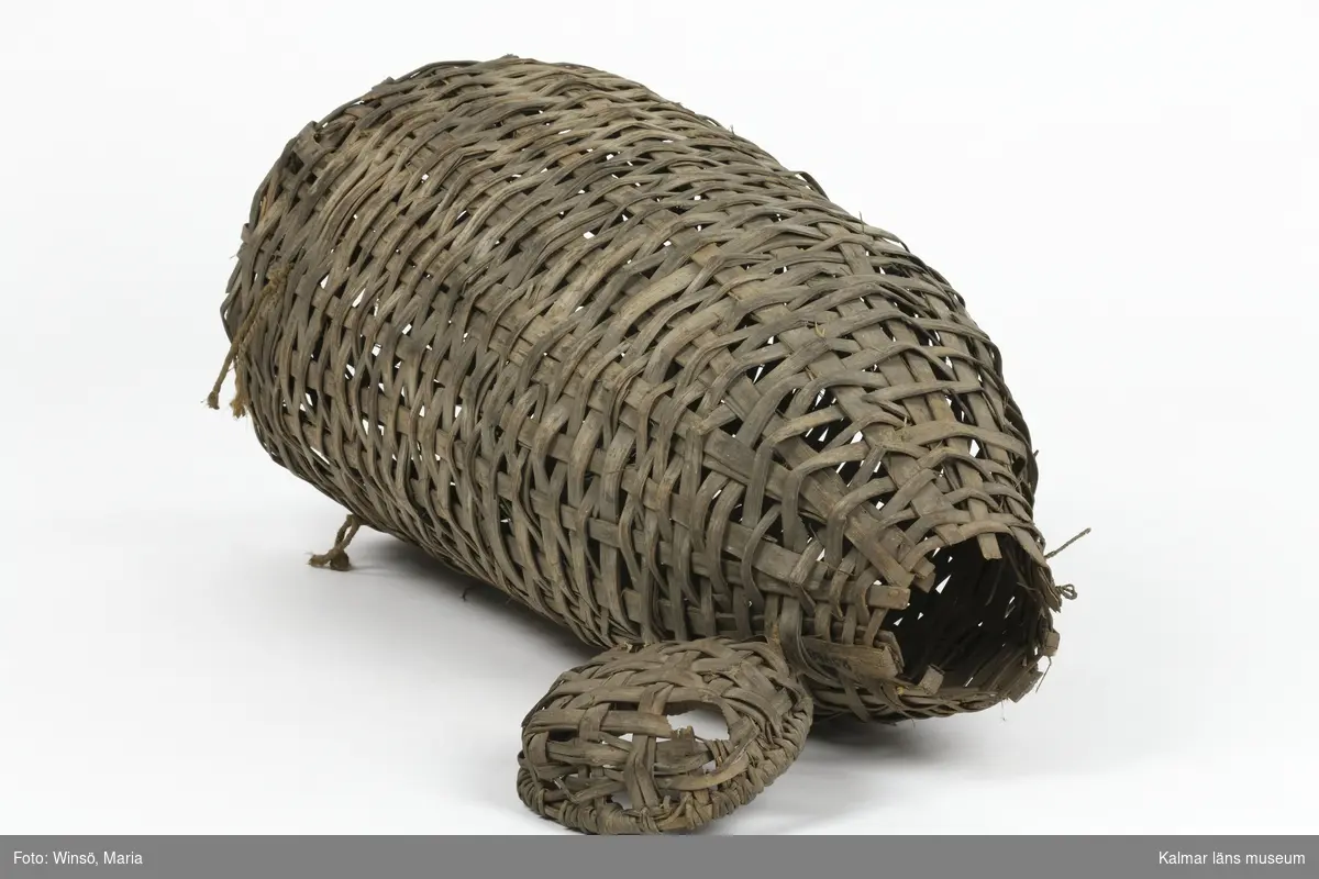 KLM 25488. Mjärde. Av flätade vidjor med vidbundet lock. Spolformad med runt tvärsnitt. En öppning i vardera ände. Vid den största öppningen en strutformad inredning. Två fastbundna snören på ena sidan.