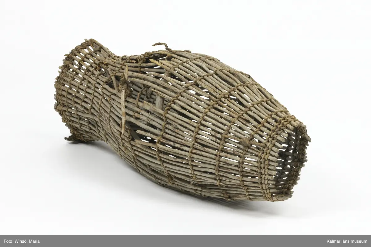 KLM 28553. Mjärde, dialektalt "ålhomma". Användes vid fiske av ål. Av vidjor sammanflätade med kedjor av rep. Spolformad och med strutliknande inredning i den cylindriska änden. I ena öppningen tygstycken. Lagad med rep på några ställen. Större skada på ena sidan.