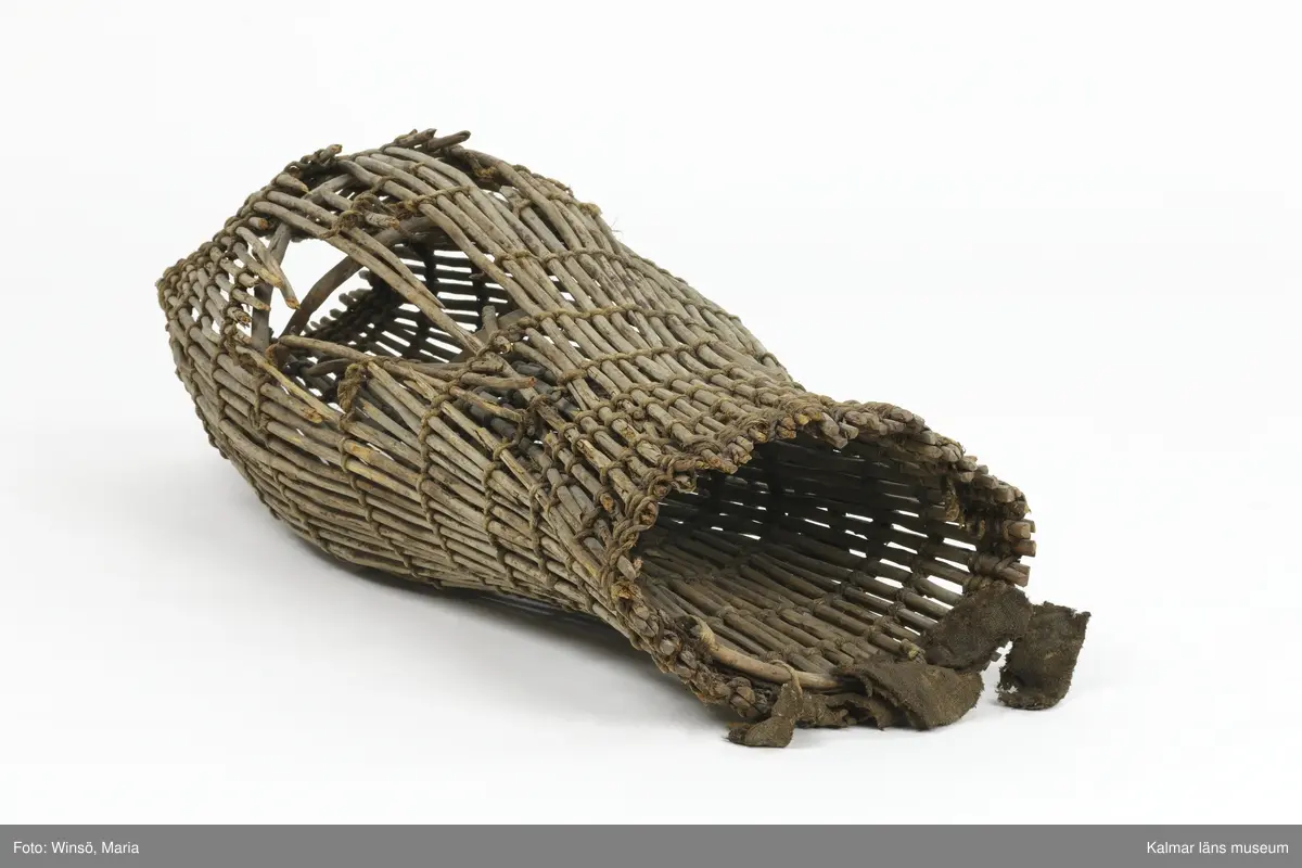 KLM 28553. Mjärde, dialektalt "ålhomma". Användes vid fiske av ål. Av vidjor sammanflätade med kedjor av rep. Spolformad och med strutliknande inredning i den cylindriska änden. I ena öppningen tygstycken. Lagad med rep på några ställen. Större skada på ena sidan.