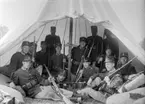 Grupporträtt. Armésoldater från I 4 och / eller I 5 regemente med gevär samlade i lägertält. Mannen direkt till vänster om tältpinnen är Henning Axfors.