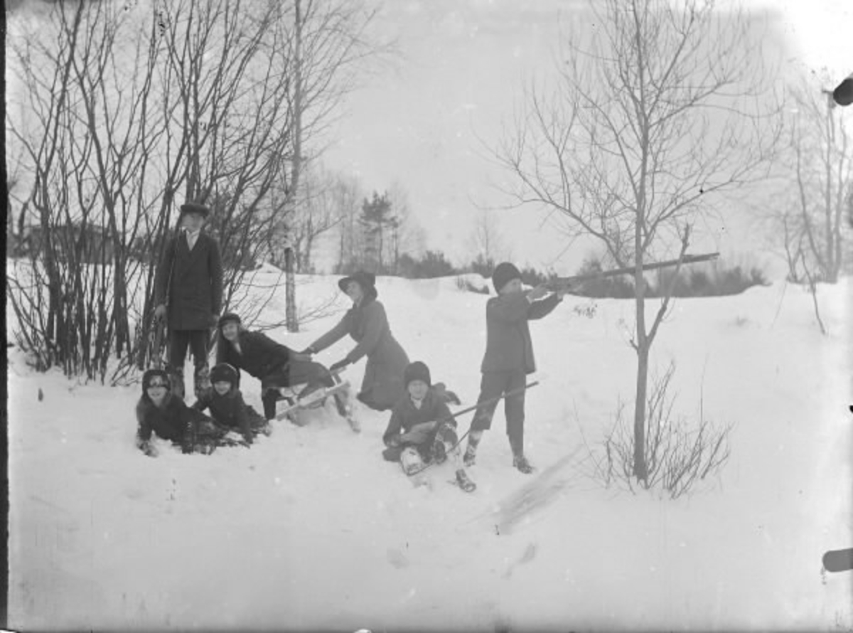 En kvinna och barn leker i snön med kälke och leksaksgevär i Drängsered. (Se även HB308, HB309)